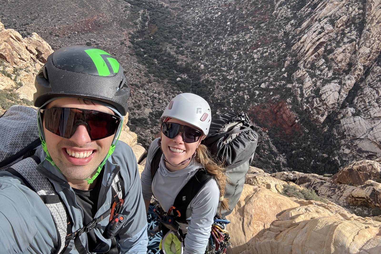 Shane Haynes and a climbing partner in helmets on a sandstone ledge high above a canyon at Red Rock